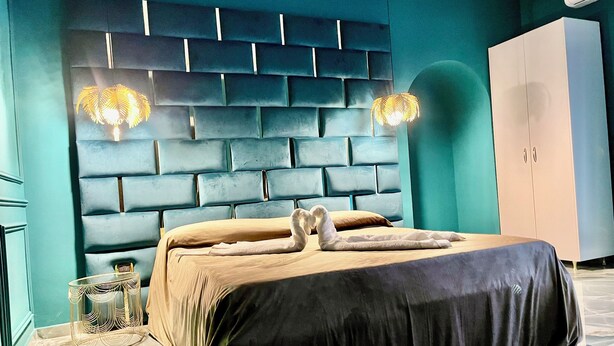 A modern bedroom with a tufted headboard, a bed with a dark cover, and a white wardrobe. - At the Naples Binario REGINA ROOM (Napoli)