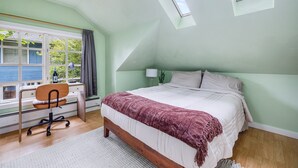 A bedroom with a bed, desk, chair, and skylight. - Sunlit Cottage Capitol Hill (Seattle)