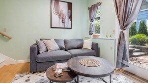 A living room with a grey sofa, a round coffee table, and a framed abstract painting on the wall. - Sunlit Cottage Capitol Hill (Seattle)