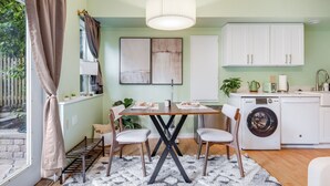 A modern kitchen with a dining table, chairs, a washing machine, and a hanging light fixture. - Sunlit Cottage Capitol Hill (Seattle)