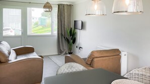 A modern living room with a sofa, a dining table, and a TV mounted on the wall. - Great property close to Freshwater East Bay, perfect for a family break. (Freshwater East)