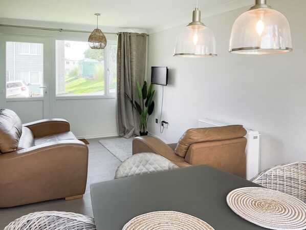 A modern living room with a sofa, a dining table, and a TV mounted on the wall.