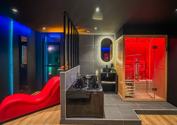 Un baño moderno con un tobogán rojo, una bañera negra y una sauna con iluminación roja.
