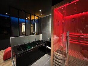 Une salle de bain moderne avec une grande baignoire noire, un miroir et une zone de douche éclairée en rouge.