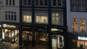 Een meerlaags gebouw met winkels op de begane grond, waaronder een bakkerij en een restaurant.