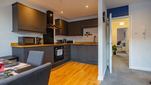 Een kleine keuken met moderne apparatuur, een eethoek met tafel en stoelen, en een duidelijke deuropening naar een andere kamer.
