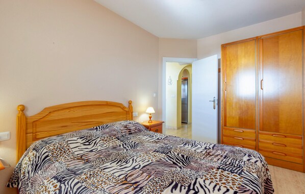 Un dormitorio con cama de madera, colcha de estampado de cebra, mesita de noche con lámpara y armario de madera.