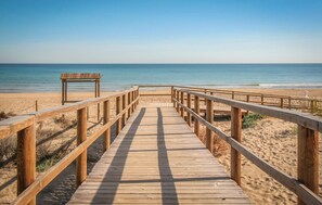 Un muelle de madera que conduce a una playa con un banco y una baranda.