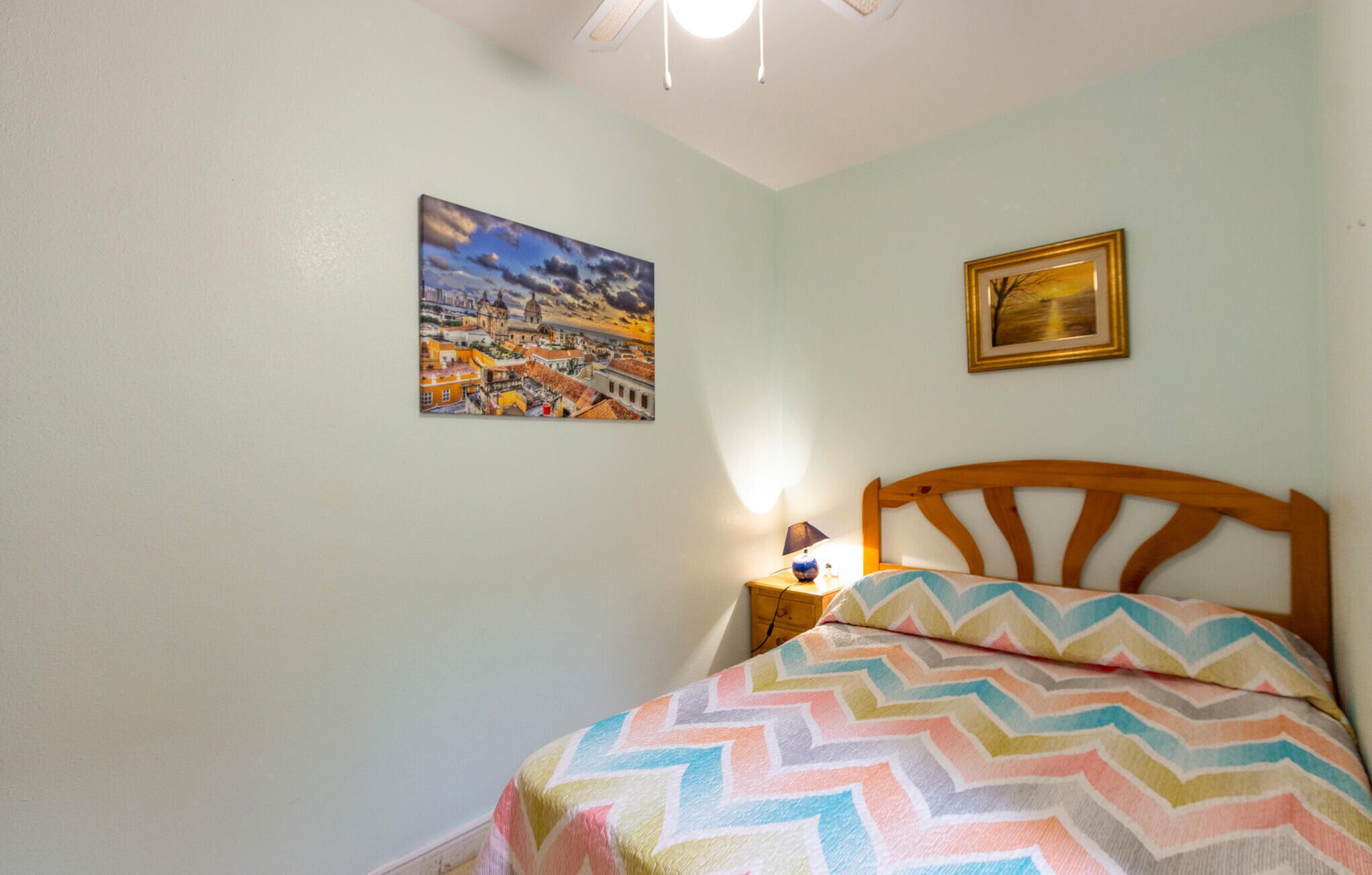 Un dormitorio con una cama, una mesita de noche, una lámpara y dos cuadros en la pared.