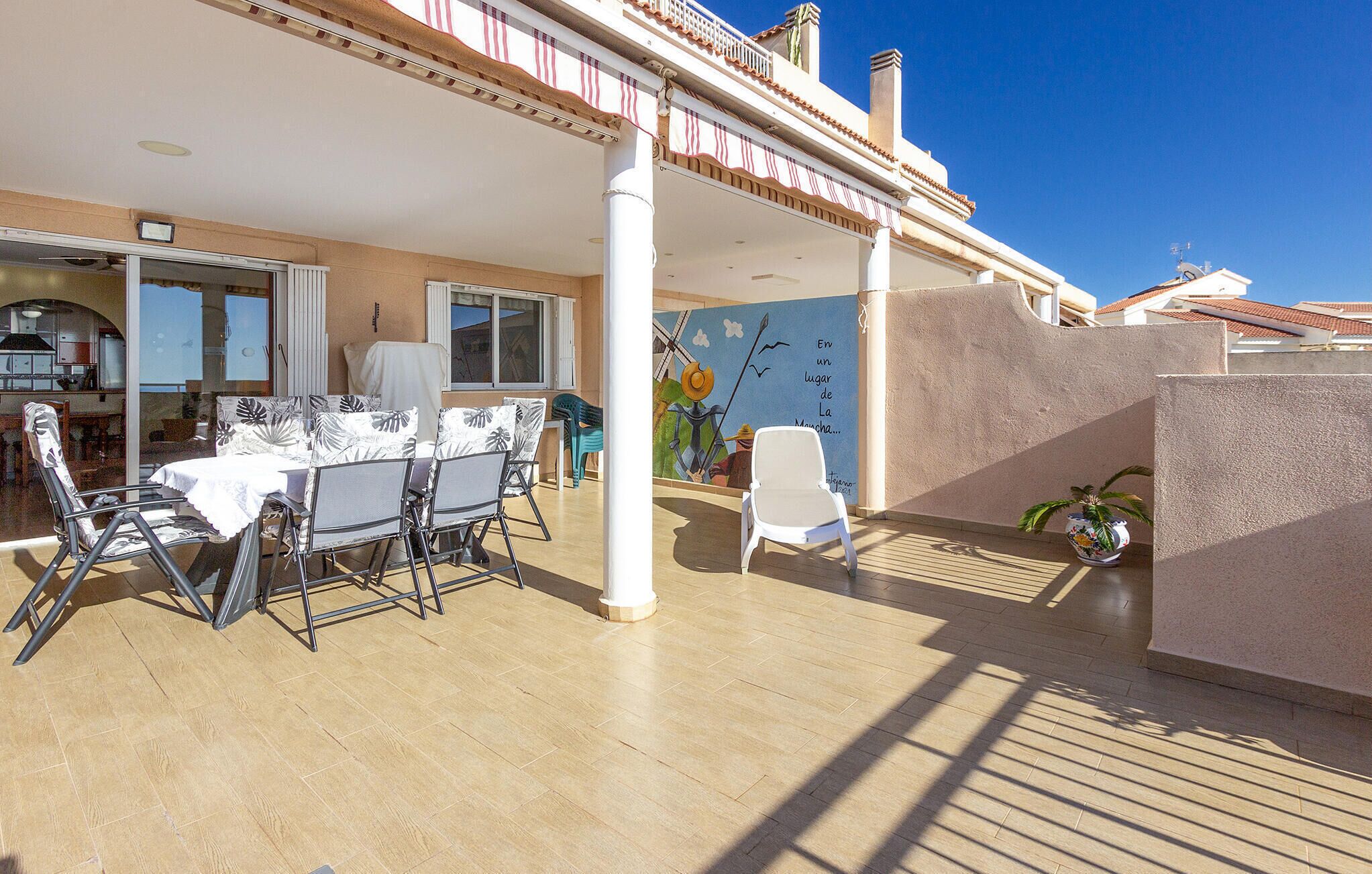 Un patio al aire libre con una mesa y sillas de comedor, una silla blanca, un mural y vistas al mar.