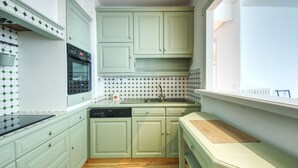 Une cuisine compacte avec des meubles de couleur vert clair, un four noir et un pare-feu en carreaux.