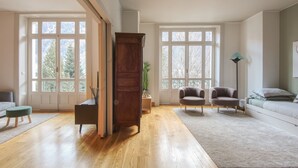 Un salon spacieux doté d’un parquet, d’une grande armoire en bois, de deux fauteuils, d’un canapé et d’un lampadaire.