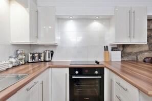 Une cuisine moderne avec des armoires blanches, un four Bosch, un plan de travail en bois et un mur en pierre.