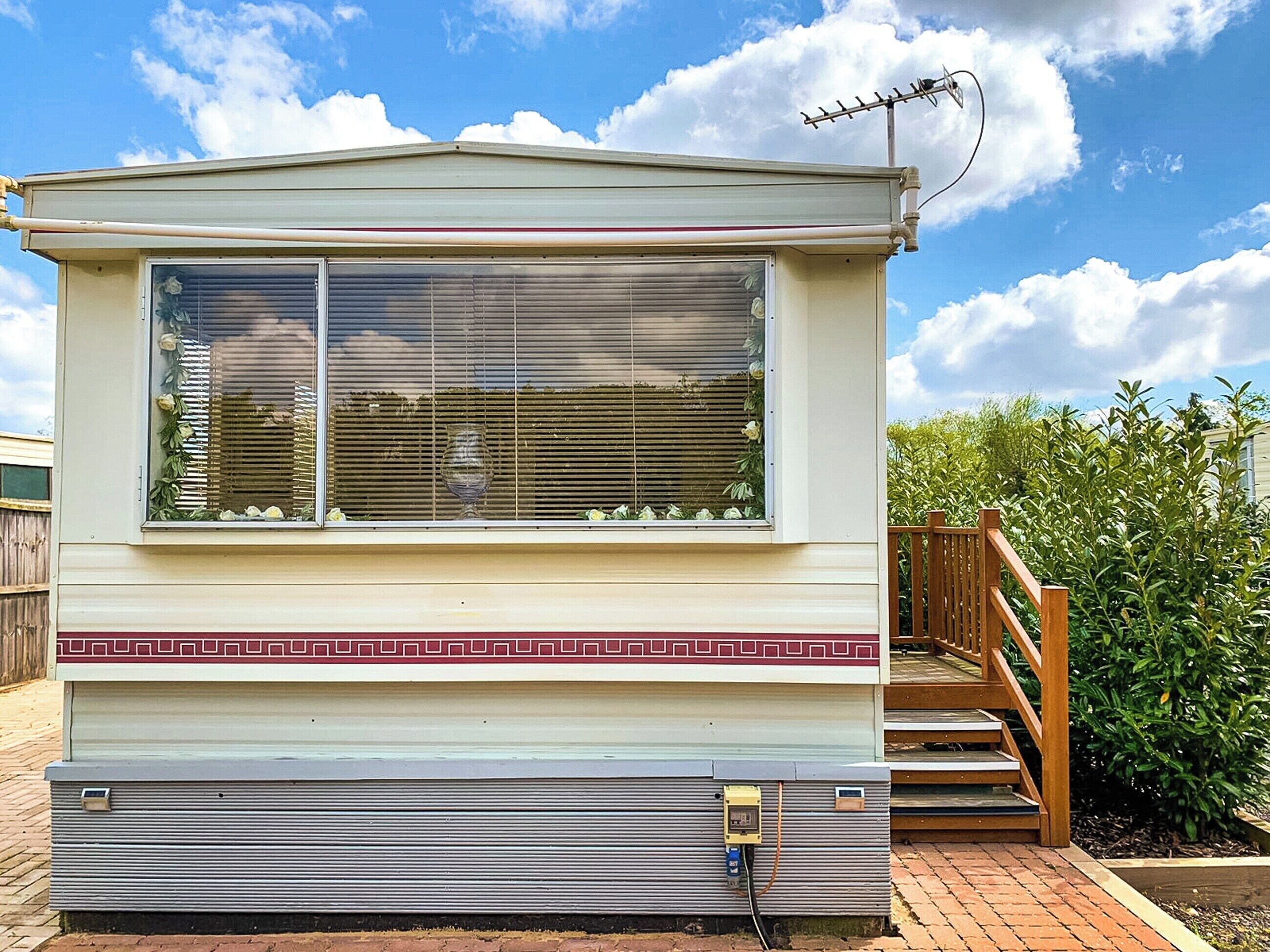 A mobile home with a large window, a wooden staircase, and a brick foundation.