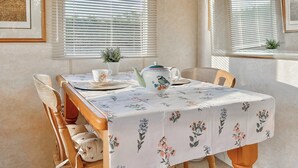 Een eettafel met een tafelkleed met bloemen, een theepot, een kopje en een kleine plant op de vensterbank.