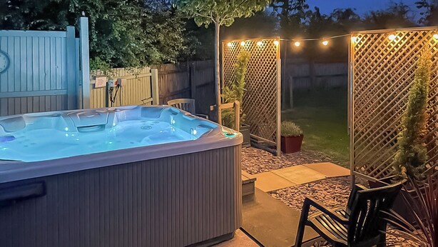 Een hottub in een achtertuin met een houten omheining, planten in potten en buitenmeubilair.