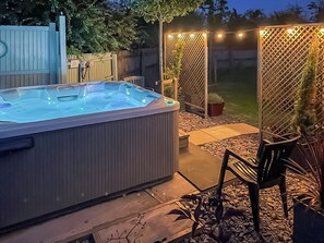 A hot tub in a backyard with a wooden fence, potted plants, and outdoor seating. - Bright spacious with a lovely garden with hot tub. (Colchester)