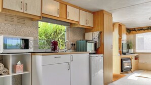 Een compacte keuken met houten kastjes, een magnetron, een waterkoker en een kleine koelkast.