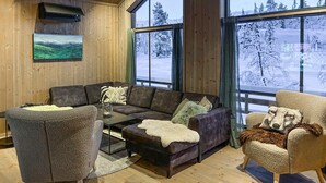 Une pièce chaleureuse avec un décor intérieur en bois, un ensemble de canapés, une table basse et une vue sur un paysage enneigé par de grandes fenêtres.
