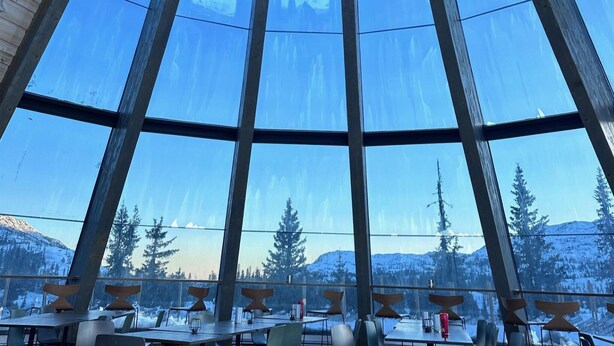 Un espace repas doté de grandes fenêtres offrant une vue sur des montagnes et des arbres enneigés.