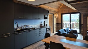 Una cocina moderna con armarios oscuros, una mesa de comedor de madera y vistas a montañas a través de amplios ventanales.