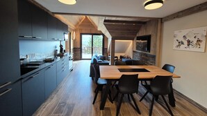 Una cocina moderna con armarios oscuros, una mesa de comedor de madera y sillas negras. Hay un amplio ventanal que ofrece luz natural y vistas al exterior.
