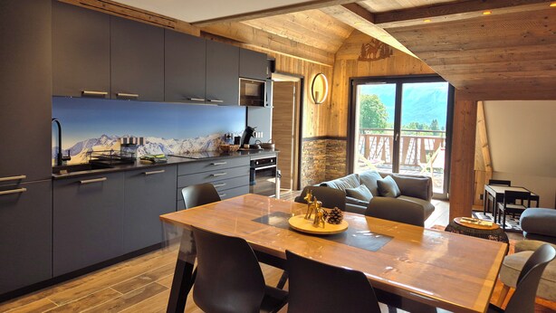 Una cocina moderna con armarios oscuros, una mesa de comedor de madera y una zona de estar acogedora con vistas a las montañas.