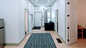 Un couloir avec un tapis à motifs, un canapé noir et un réfrigérateur.