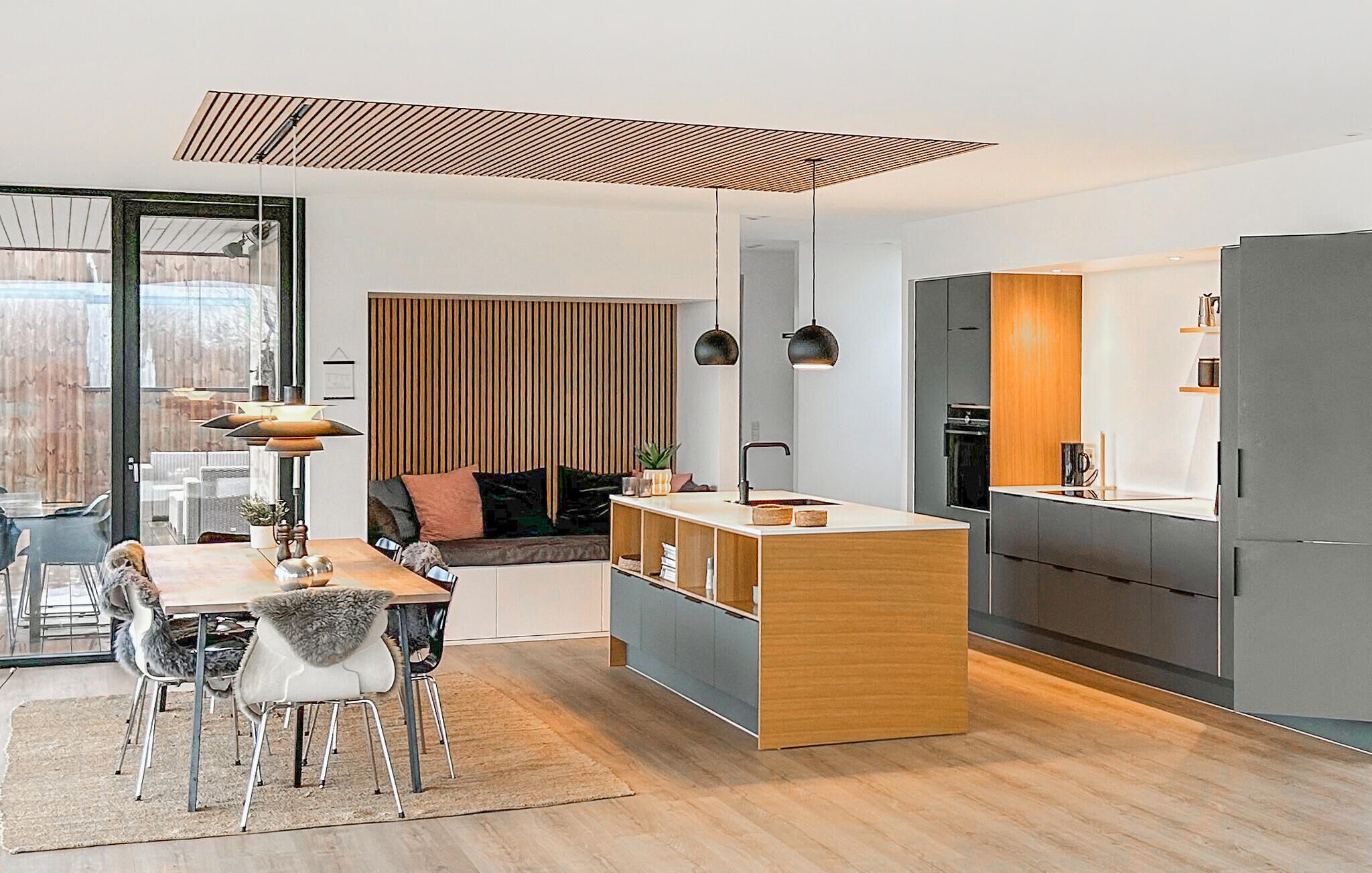 A modern kitchen with a central island, a dining area with a table and chairs, and a cozy seating area with a sofa and cushions.