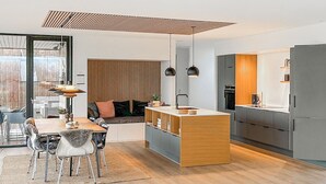 Une cuisine moderne dotée d’un îlot central, un coin repas avec une table et des chaises, et un espace salon confortable avec un canapé et des coussins.