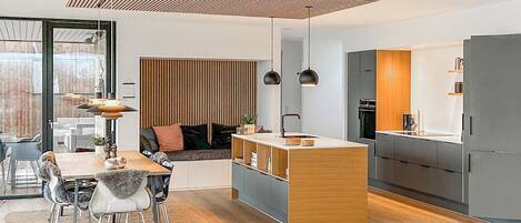 A modern kitchen with a central island, a dining area with a table and chairs, and a cozy seating area with a sofa and cushions.