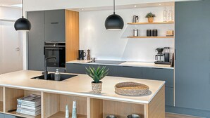 Une cuisine moderne dotée d’un îlot central, de luminaires suspendus noirs et d’appareils électroménagers intégrés.