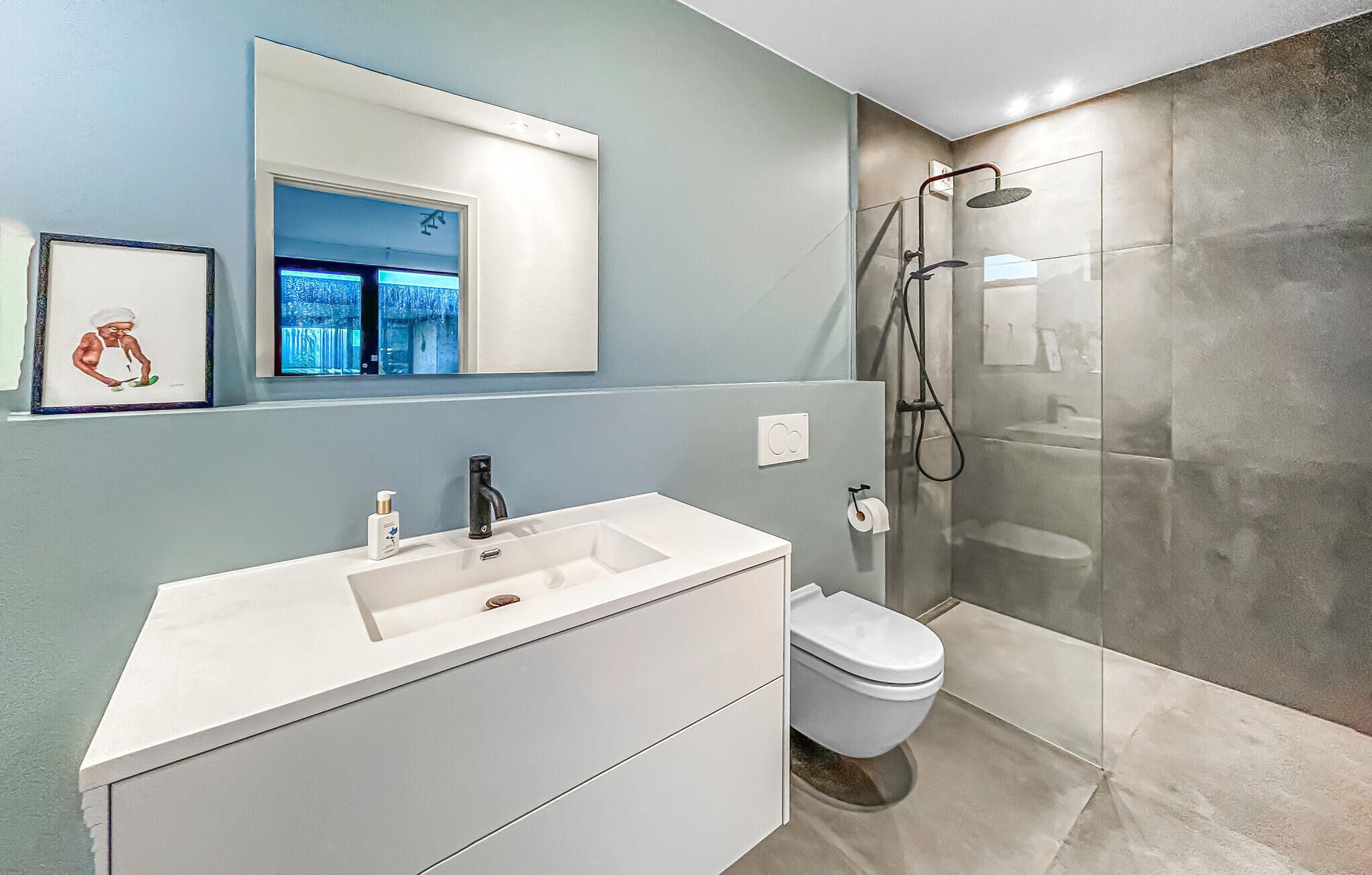 Un baño moderno con lavamanos blanco, inodoro y ducha con mampara de vidrio.