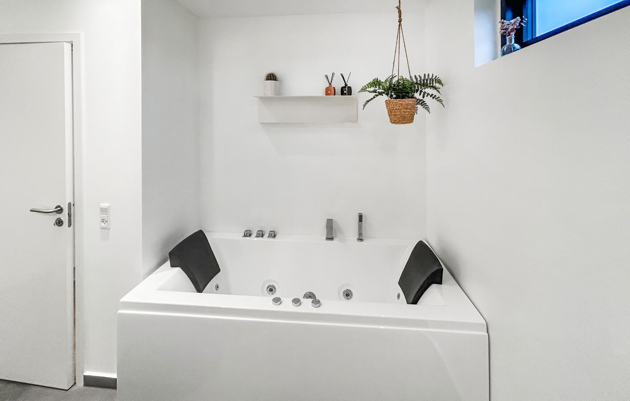 Un baño moderno con una bañera independiente, un pequeño estante con adornos y una planta colgante.