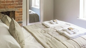 Una cama bien hecha con edredón blanco, una pared de ladrillo y un espejo que refleja una ventana.