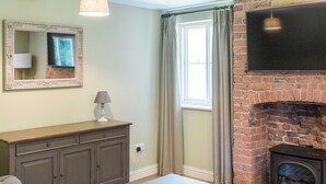 Una sala de estar con chimenea, televisor montado en la pared, una mesa con controles remotos y una ventana con cortinas.