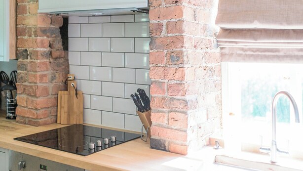 Una cocina con pared de ladrillo, azulejos blancos, encimera de madera, estufa y ventana con cortina.