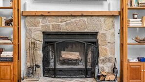 Una chimenea de piedra con repisa, flanqueada por estanterías de madera y un televisor en la parte superior.