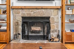 A stone fireplace with a mantel, flanked by wooden bookshelves and a television above.