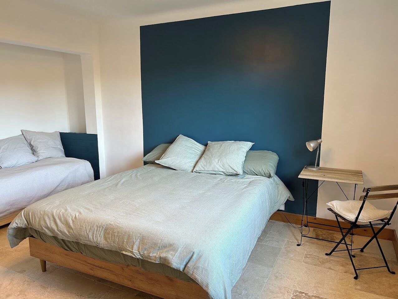 A bedroom with a large bed, two smaller beds, a desk with a chair, and a blue accent wall.