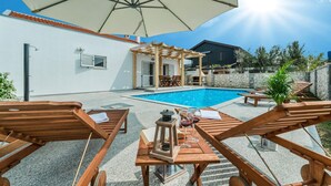 A poolside area with wooden loungers, a pergola, and a stone wall. - Beautiful home in Privlaka (Privlaka)