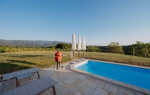 A swimming pool with a barbecue grill and umbrellas, surrounded by a grassy area and mountains in the background. - Lovely home in Stubicke Toplice with sauna (Stubicke Toplice)