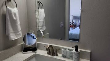 A bathroom with a large mirror, a sink, and two towel rings.