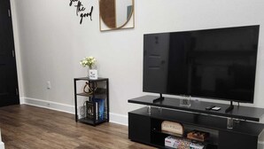 Una sala de estar moderna con un televisor de pantalla plana, un mueble de entretenimiento negro, un otoman redonda y un espejo decorativo en la pared.