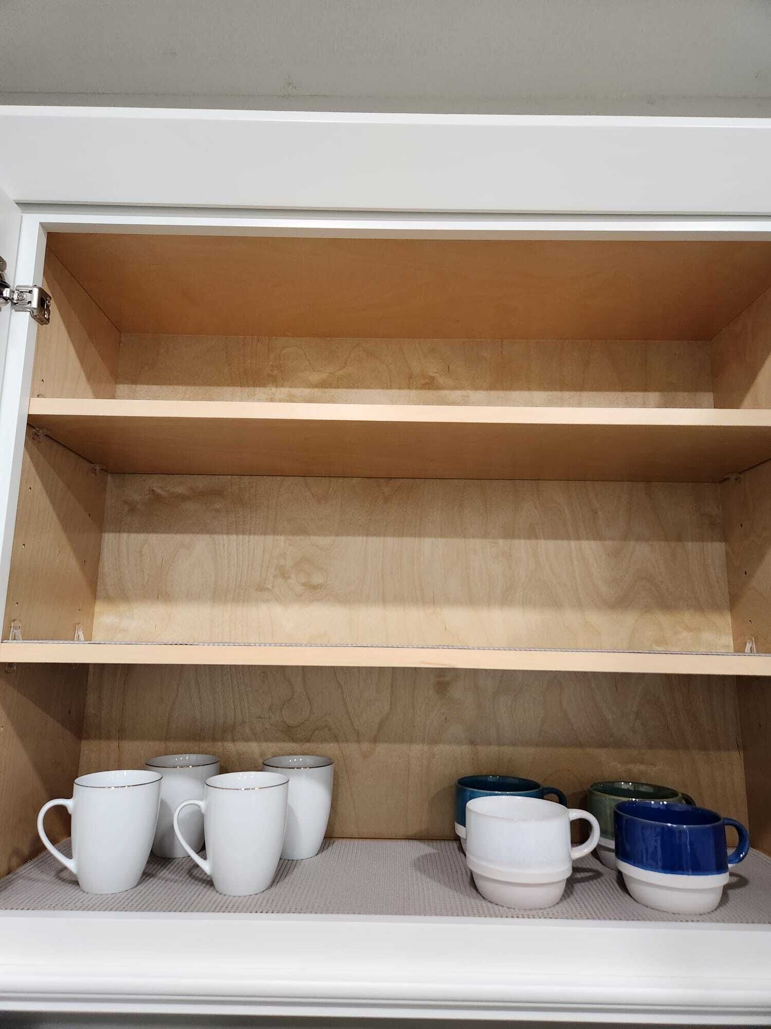 A wooden cabinet with two shelves, one of which is empty and the other holding several white and blue mugs.