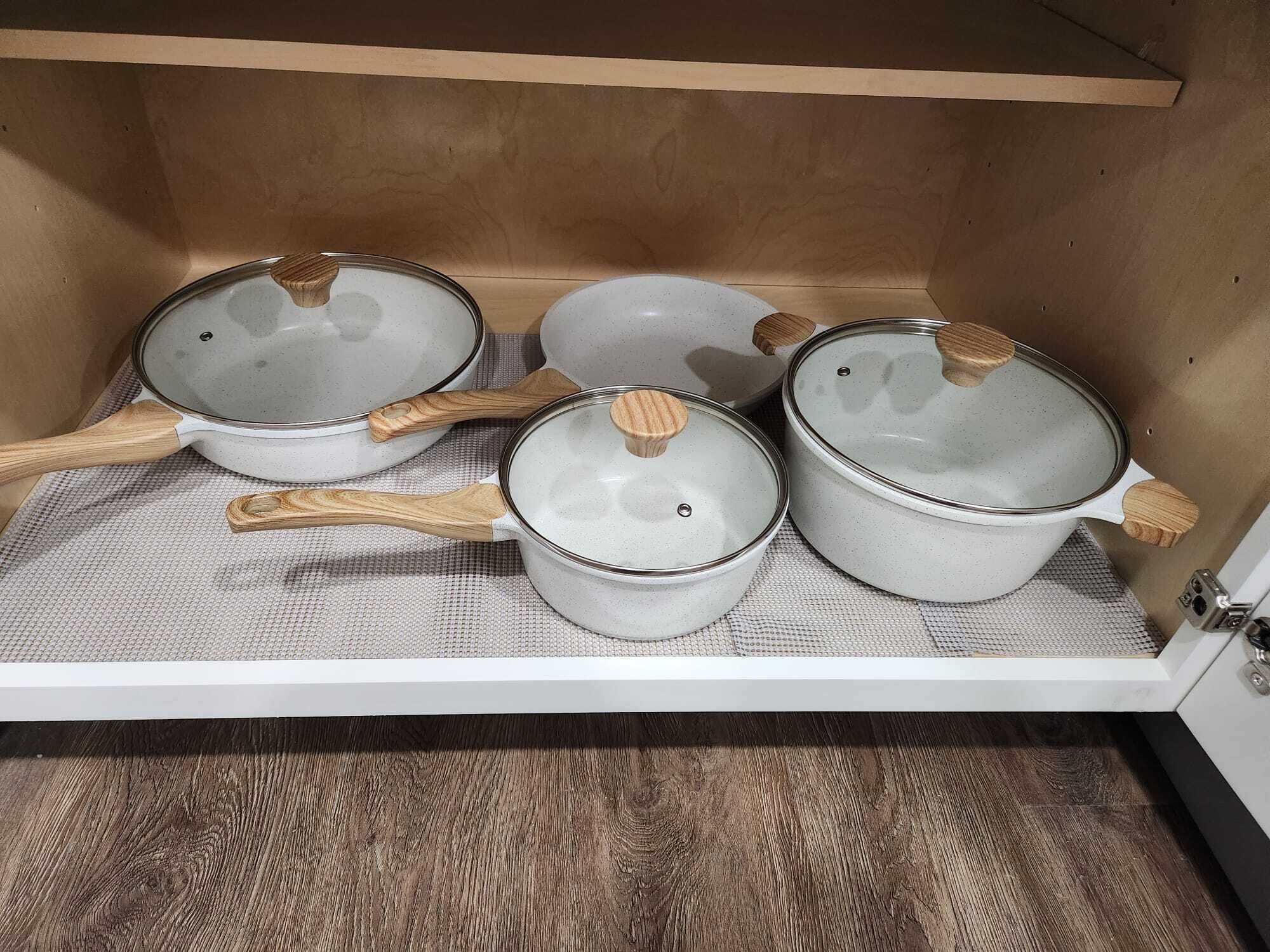 A kitchen cabinet with three pots and two wooden spoons.
