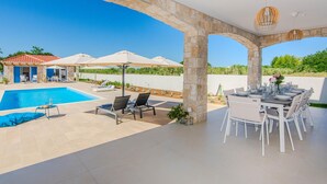 A poolside area with a stone archway, a dining table set for six, and a pool with lounge chairs. - Stunning home in Privlaka with private swimming pool, can be inside or outside (Privlaka)