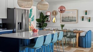 Cocina moderna con una isla central, sillas azules y lámparas de mimbre colgantes.