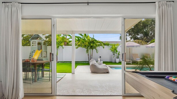 Una sala de estar moderna con mesa de billar, zona de juegos con tobogán y terraza con mobiliario exterior.
