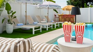 Zona junto a la piscina con sillones, sombrillas y una mesa con lámpara.